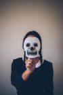 Portrait of girl in black dress holding skull mask in front of face — Stock Photo