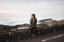 Frau sitzt am Straßenrand über nebliger Landschaft — Stockfoto
