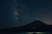 Silhouette of tourist against of starry sky above mountain silhouette at night — Stock Photo