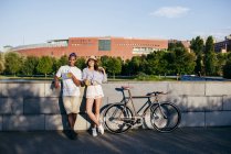 Couple with drinks and bike leaning on parapet — Stock Photo