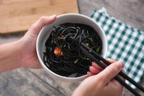 Couper les mains en tenant un bol avec des spaghettis noirs et des baguettes — Photo de stock