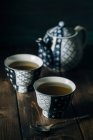 Two porcelain cups of hot tea by pot on wooden table. — Stock Photo