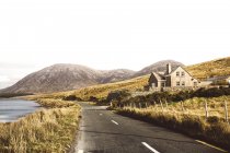 Peaceful landscape with lonely road and house on background of mountains. — Stock Photo