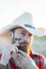 Portrait d'homme barbu en chapeau de cow-boy rasant avec un rasoir vintage à double bord et regardant la caméra — Photo de stock