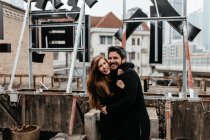 Smiling couple in black apparel cuddling on rooftop. — Stock Photo