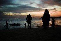 MALAYSIA- May 1, 2016:  Silhouettes of people with kids on beach over sunset sky on background. — Stock Photo