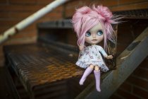Nahaufnahme einer modernen Puppe mit rosa Haaren, die auf einer Metalltreppe sitzt — Stockfoto