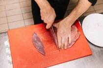 Blick auf männliche Hände, die in der Restaurantküche Fleisch an Bord schneiden — Stockfoto