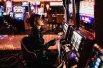 Vista lateral da mulher sentada no cassino e jogando slot machine. — Fotografia de Stock