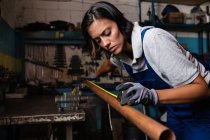 Mecânico feminino medindo tubo de ferro enferrujado na garagem — Fotografia de Stock