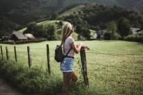 Back view of woman leaning on wooden fence at countryside. — Stock Photo