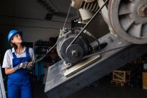 Mecânico feminino operando um guincho para levantar o motor do compressor na garagem — Fotografia de Stock