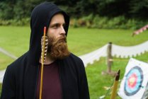 Серьезный бородатый мужчина, позирующий с луком — стоковое фото