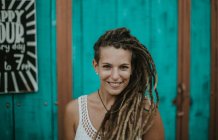 Portrait of smiling woman with dreadlocks posing over turquoise wooden wall and looking at camera. — Stock Photo