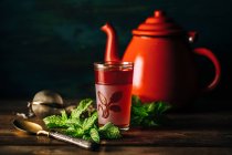 Verre à thé arabe rouge avec théière rouge sur table en bois . — Photo de stock