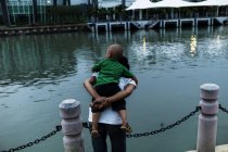 MALAYSIA- April 23, 2016: Rear view of man giving kid piggyback on background of river. — Stock Photo