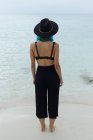 Visão traseira da menina de cabelos azuis irreconhecível em sutiã preto e calças de pé perto do mar. — Fotografia de Stock