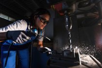 Mecânico feminino em óculos de proteção usando pistola de sopro de ar para limpar aparas de broca tipo coluna — Fotografia de Stock