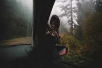 Gambe di persona che mette fuori del finestrino dell'automobile nella foresta . — Foto stock