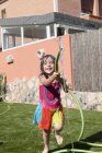 Mädchen spielt an heißen Sommertagen mit Schlauch im Garten — Stockfoto