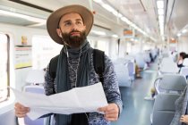 Porträt eines bärtigen Mannes mit Karte, der Musik im Eisenbahnwaggon hört — Stockfoto