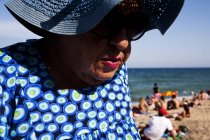 BARCELONA, SPAIN - 10 July, 2011: Portrait of senior woman wearing hat and sunglasses on background of beach and sea. — Stock Photo