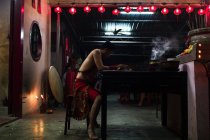 KAULA LUMPUR, MALASIA - 26 DE FEBRERO DE 2016: Hombre vestido de mujer sentado a la mesa sobre fondo de linternas - foto de stock