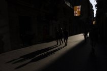 Pessoas andando no beco da cidade com a luz solar fazendo longas sombras . — Fotografia de Stock