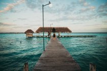 Back view of man walking on wooden pier on turquoise water of ocean. — Stock Photo