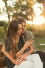 Retrato de niño abrazando novia navegando teléfono inteligente en el banco en el parque - foto de stock