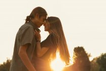 Vista lateral do casal abraçando e olhando cara a cara ao pôr do sol — Fotografia de Stock