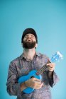 Смеющийся бородатый мужчина играет на традиционной гитаре укулеле на синем фоне — стоковое фото