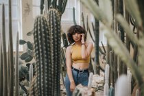 Chica morena sensual en top amarillo posando entre cactus - foto de stock