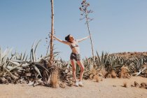 Young girl in bikini top and shorts holding trees in sunlight in desert — Stock Photo