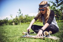 Молодая женщина затягивает орехи в грузовиках скейтборда на газоне — стоковое фото