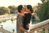 Retrato de novio abrazando novia y besándose en la nariz en las escaleras en el parque sobre el lago en el telón de fondo - foto de stock