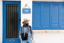 Homem barbudo de chapéu inclinado na fachada sob placa com palavra de casa . — Fotografia de Stock