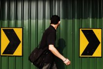 MALAYSIA- Mart 31, 2016: Vista lateral del hombre caminando sobre fondo de valla metálica verde con flechas de dirección . - foto de stock