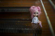 Крупним планом вид на рожево-волохату сучасну ляльку, що сидить на металевих сходах — стокове фото