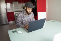 Retrato del hombre barbudo sentado en la mesa y usando el ordenador portátil - foto de stock