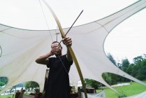 Чоловік практикує стрільбу з лука на тлі навісу — стокове фото