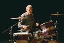 Зрелый человек играет на барабанах против черного — стоковое фото
