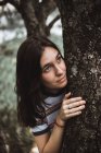 Bruna donna guardando lontano mentre si nasconde dietro tronco d'albero — Foto stock