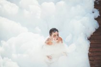 Criança alegre brincando na espuma branca — Fotografia de Stock