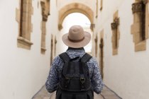 Vista posteriore del turista maschio con zaino che indossa cappello e in piedi in strada . — Foto stock