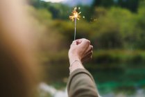 Crop hand holding sparkler on nature — Stock Photo