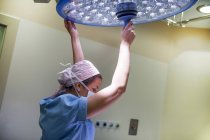 Vista lateral do médico feminino ajustando a luz na sala de cirurgia . — Fotografia de Stock