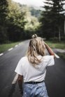 Rückansicht einer blonden Frau, die auf einer Rute durch den Wald geht — Stockfoto