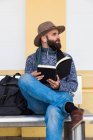Избитый мужчина сидит с книгой в руках, слушая музыку и отводя взгляд — стоковое фото