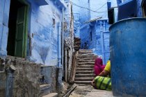 Colorful narrow street painted in blue with people sitting. — Stock Photo